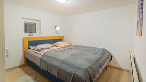 A bedroom with a bed, a nightstand, a wall-mounted light, a window, and a ceiling light. - Cute gallery flat in Budapest Pearl  (Budapest)
