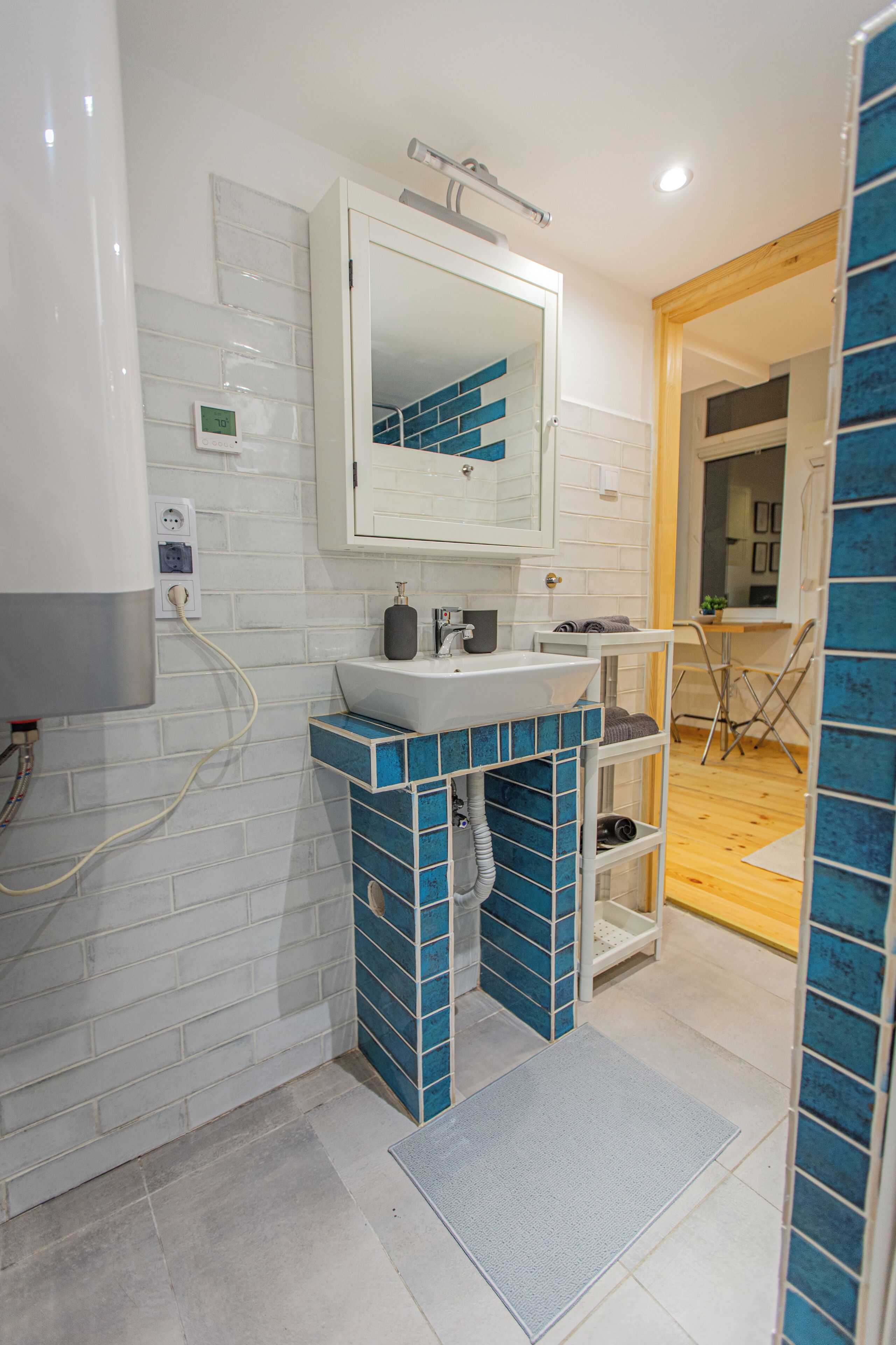 A bathroom with a white sink, blue-tiled vanity, and a mirror above it.