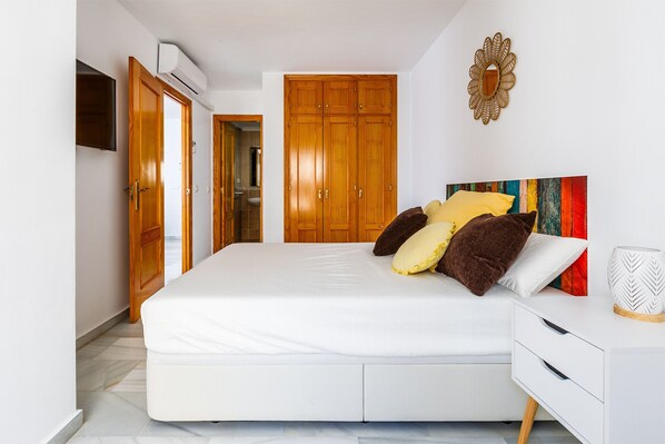 Een slaapkamer met een bed, een houten kledingkast en een aan de muur bevestigde televisie.