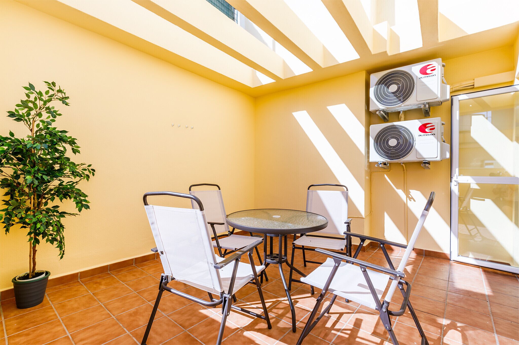 Eine Terrasse mit rundem Tisch und Stühlen, einem Blumentopf und zwei Klimaanlagen.