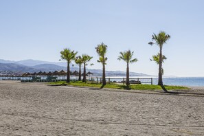 Une plage bordée de palmiers, une clôture en bois et une rangée de constructions aux toits de chaume.