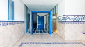 Ein Korridor mit Schachbrettboden, Wänden im blauen und weißen Muster und einer blauen Tür am Ende.