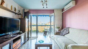 Ein Wohnzimmer mit Fernseher, Sofa und einem Balkon mit Blick auf Gebäude.