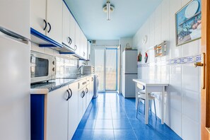 Een keuken met witte kastjes, een magnetron, een koelkast en een raam met uitzicht.