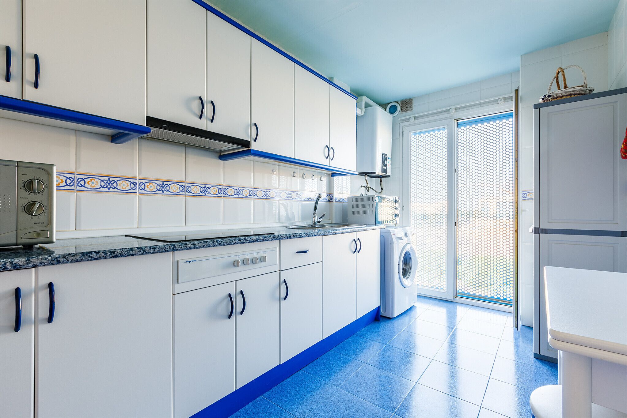 A kitchen with white cabinets, blue accents, a washing machine, and a window with a view.