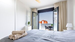 Une chambre d’hôtel moderne avec un grand lit, une vue sur la ville par une porte ouverte et une petite table avec des chaises.