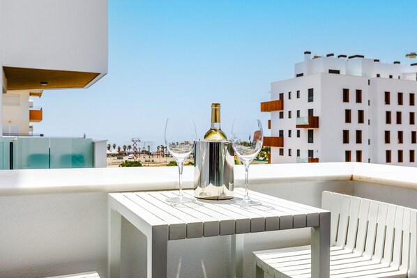 Ein Balkon mit Tisch, zwei Stühlen, einer Flasche und zwei Gläsern.