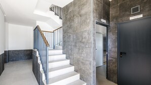 Un intérieur moderne avec un escalier, une porte sombre portant l’inscription « CONTADORES DE LUZ » et une enseigne indiquant « MERCADO ».