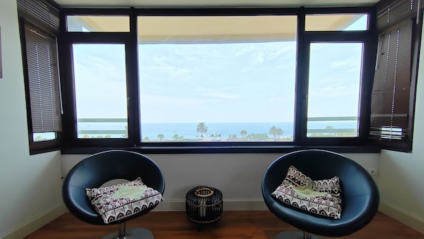 Zwei schwarze Stühle mit gemusterten Kissen, ein kleines Dekorationsstück und Blick aufs Meer durch große Fenster.