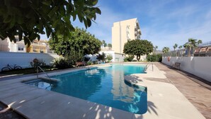 Ein Swimmingpool mit klarem, blauem Wasser, umgeben von einer weißen Mauer, Bäumen und einem Gebäude im Hintergrund.