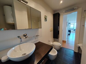 A modern bathroom with a large mirror, a vessel sink, a toilet, and a dark wooden vanity.