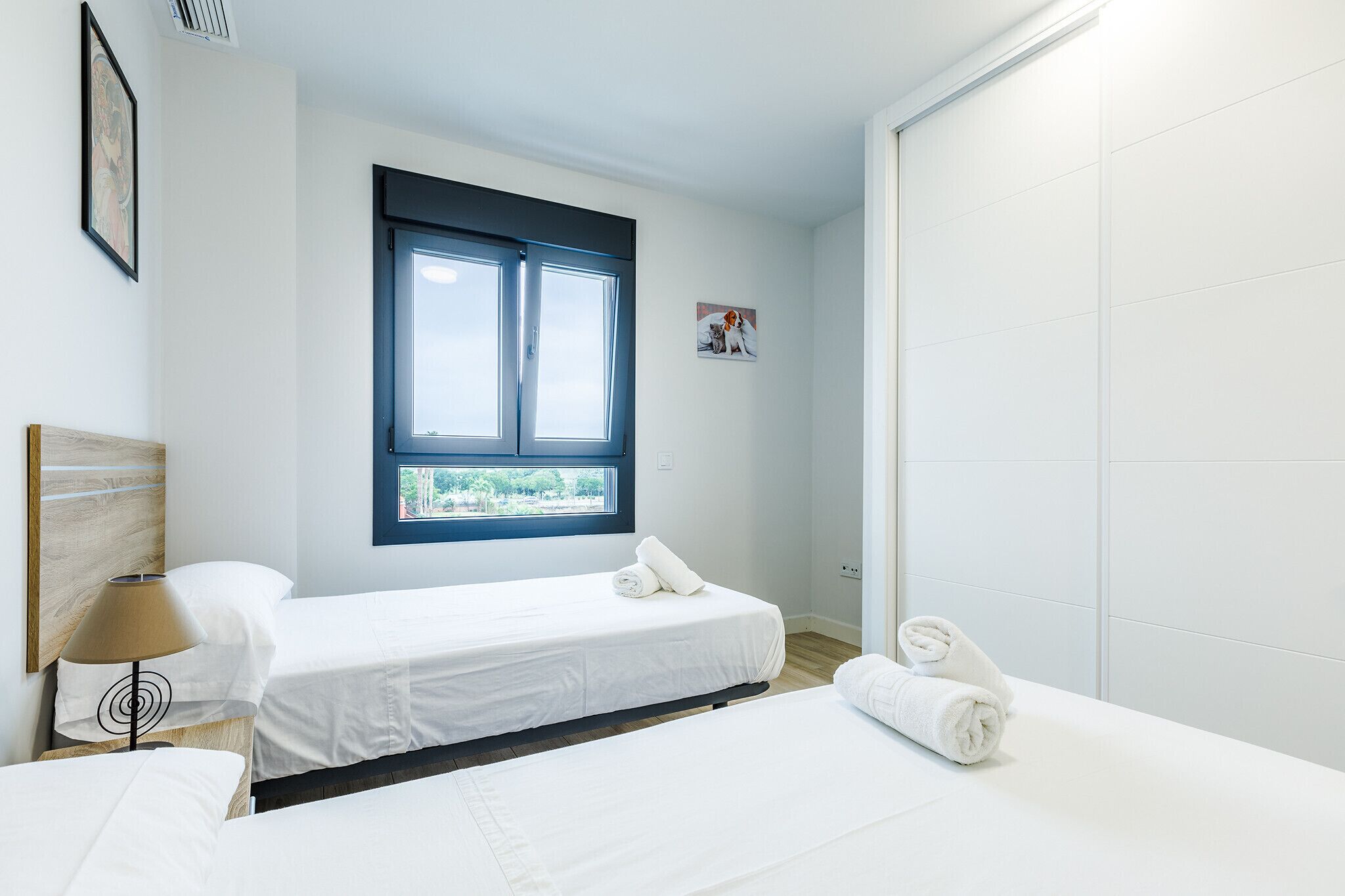 Une chambre d’hôtel avec deux lits simples, une fenêtre, un tableau accroché au mur et une table de chevet avec une lampe.