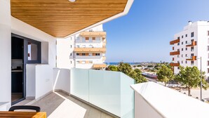 Un balcon doté d’un plafond en bois, offrant une vue sur la mer et, en arrière-plan, des bâtiments modernes.