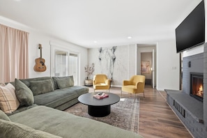 A modern living room with a sofa, two armchairs, a coffee table, a fireplace, and a guitar on the wall.