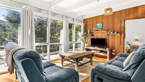 Una sala de estar moderna con un televisor grande, asientos cómodos y vistas al exterior.