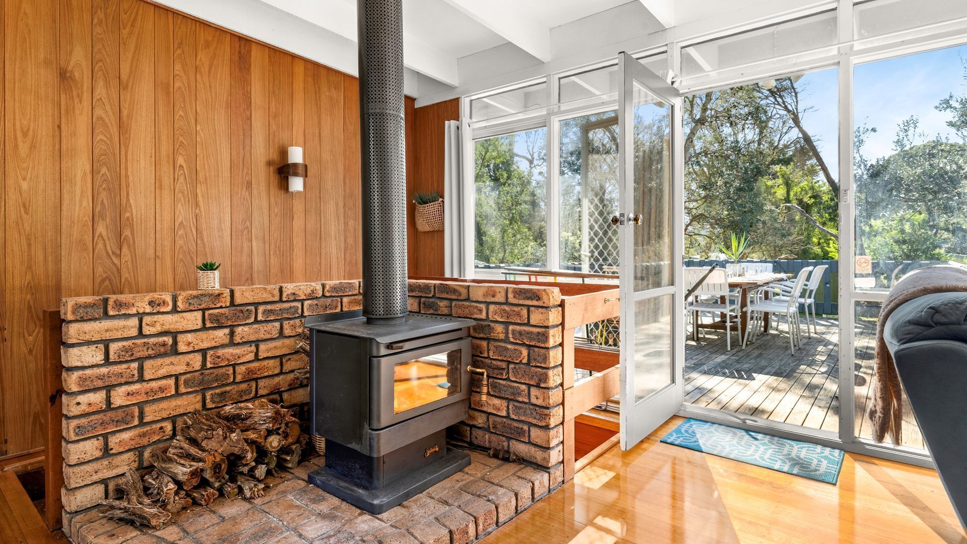A modern interior with a wood-burning stove, a wooden wall, and a glass door leading to an outdoor patio.
