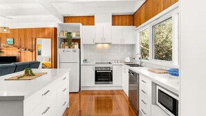 Una cocina moderna con armarios blancos, horno integrado, lavavajillas y un amplio ventanal con vistas al exterior.