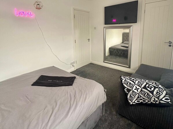 A bedroom with a bed, a chair, a neon 'love' sign, a TV, and a wardrobe. - The Hideaway Home BD5 - 2 Bed Lovely Modern House (Bradford)