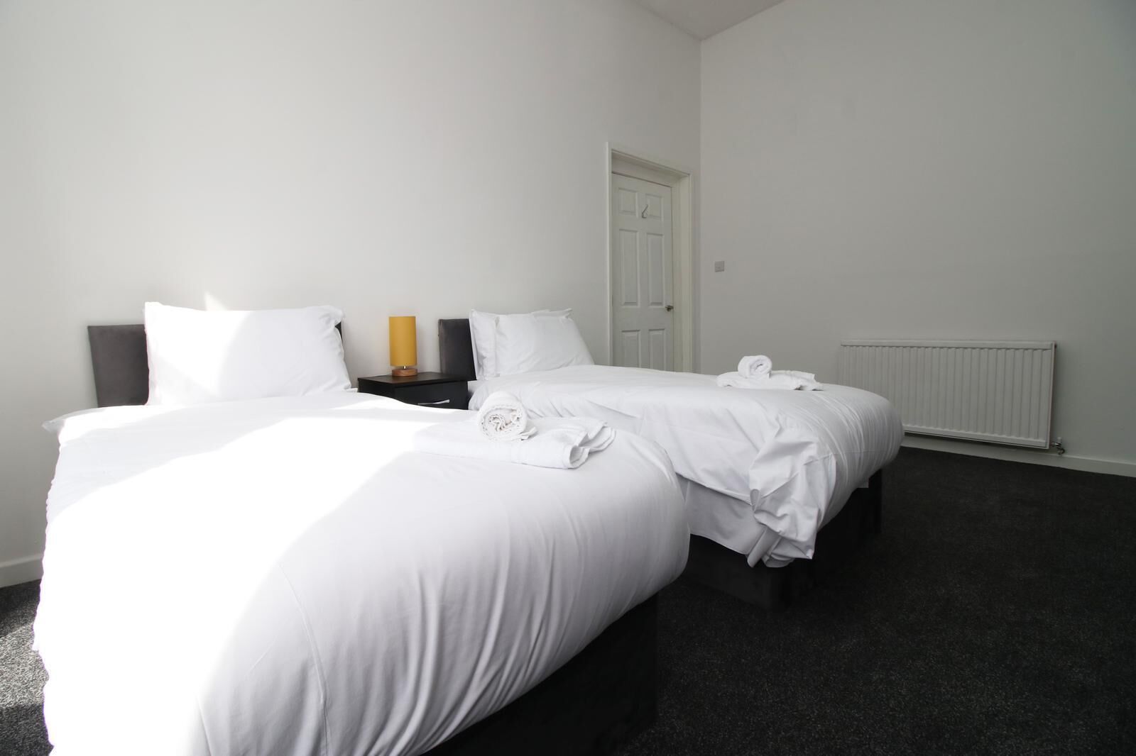 Ein Hotelzimmer mit zwei Betten, einem Nachttisch, einem Heizkörper und einer Tür.