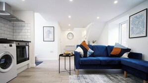 Een moderne woonkamer met een blauwe bank, een wasmachine en een keukenhoek.