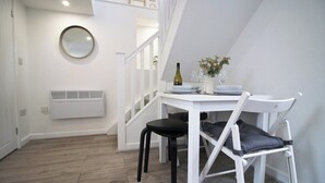 Een kleine eethoek met een witte tafel en stoelen, een witte radiator en een trap naar een hoger gelegen verdieping.