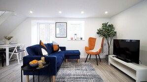 Een moderne woonkamer met een hoekbank, een televisie en een eetgedeelte met een witte tafel en stoelen.