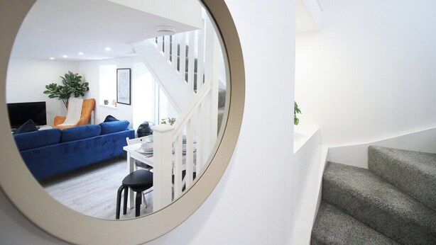 Een moderne woonkamer met een blauwe bank, een eettafel en een trap.