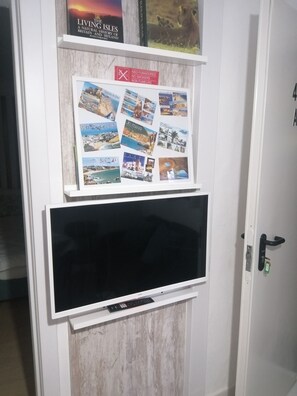 A wall-mounted television with a remote control, a framed collage of travel photos, and a book titled "The Living Isles".