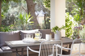 A patio with a wicker table, white chairs, a cushioned bench, a pitcher, glasses, a tray, and a vase with flowers.