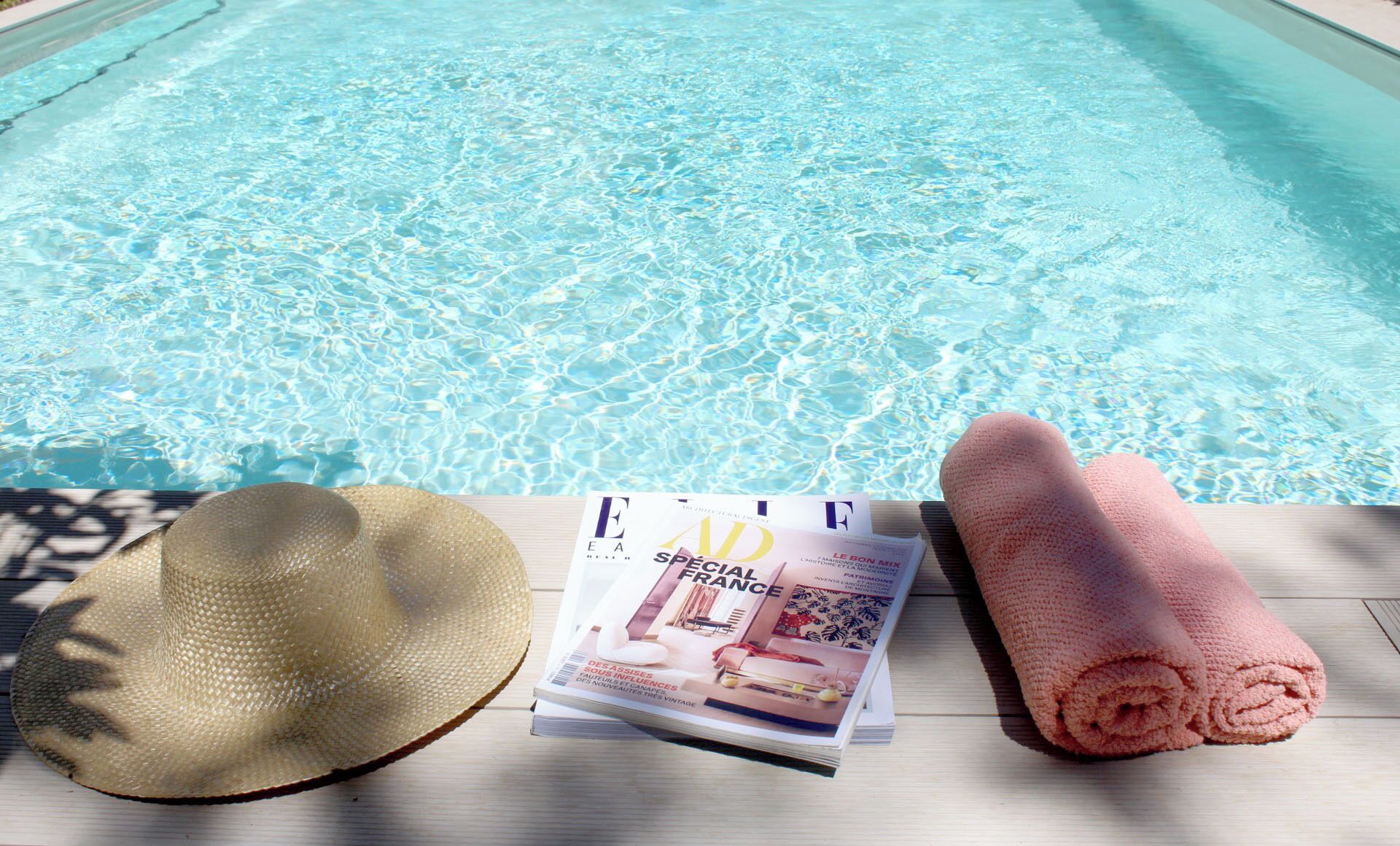 A poolside setting with a magazine, a straw hat, and a rolled towel.