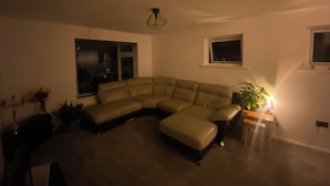 A living room with a sectional sofa, a small table with a lamp, and a potted plant.