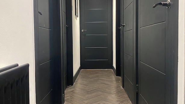 A hallway with dark wooden doors, a herringbone-patterned floor, and a radiator on the left.