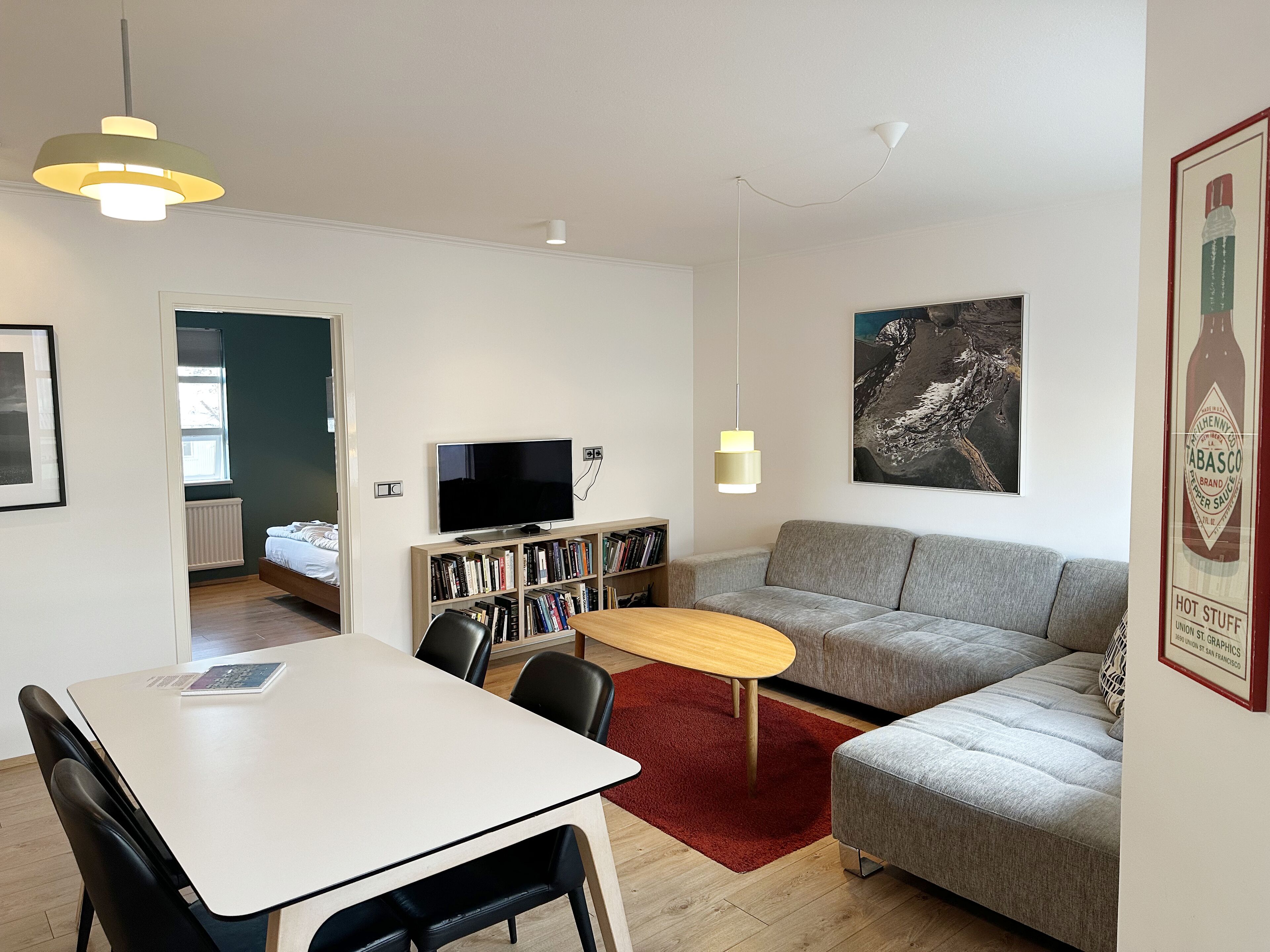 A modern living room with a sofa, a dining table, and a TV. There is a bookshelf and a red rug.