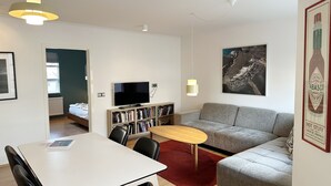 Ein modernes Wohnzimmer mit einer Couch, einem Esstisch und einem Fernseher. Ein Bücherregal und ein roter Teppich sind ebenfalls vorhanden.