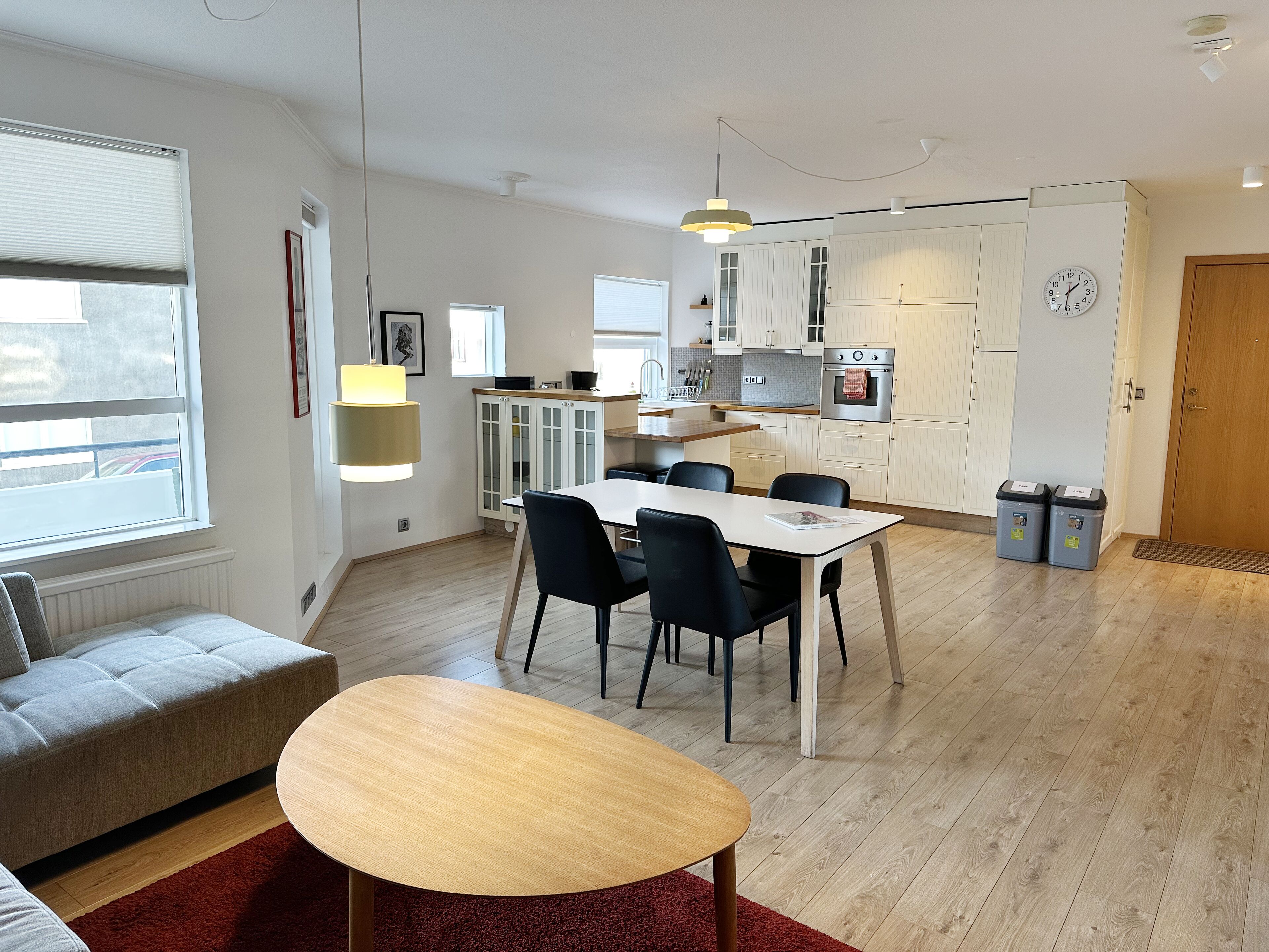 A modern kitchen with white cabinets, a dining area with a table and chairs, and a red rug.
