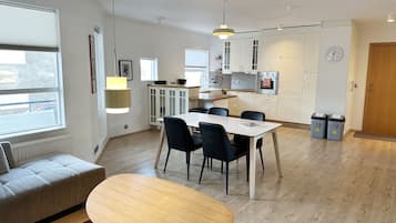 A modern kitchen with white cabinets, a dining area with a table and chairs, and a red rug.