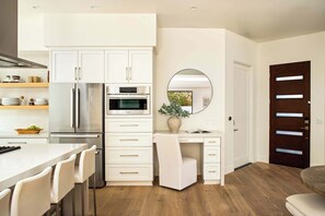 A modern kitchen with white cabinetry, stainless steel appliances, and a dining area with a marble countertop and white chairs. - Sleek Beach House | Spa, Fire Pit & Ocean Views (Encinitas)