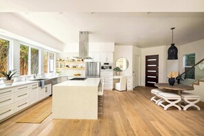 Una cocina moderna con armarios blancos, una isla grande y un comedor con taburetes blancos.