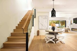 A modern interior with a wooden staircase, a round dining table with white stools, and a black pendant light.
