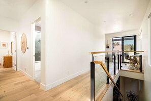 A modern interior with a wooden floor, a glass door leading to a balcony, and a staircase with a glass railing. - Sleek Beach House | Spa, Fire Pit & Ocean Views (Encinitas)
