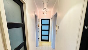 A narrow hallway with a wooden floor, a black mat at the entrance, and a door with frosted glass panels. - Immaculate 3-bed Apartment in London (London)