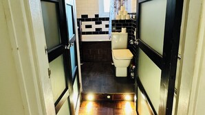 A narrow hallway leading to a bathroom with a toilet, sink, and a window. - Immaculate 3-bed Apartment in London (London)