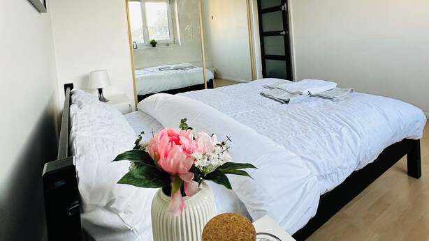 A hotel room with a bed, a bedside table with a vase of flowers, a candle, and a suitcase. - Immaculate 3-bed Apartment in London (London)
