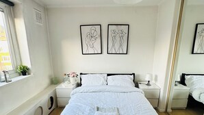 A bedroom with a large bed, two bedside tables, a window with a view, and two wall-mounted artworks. - Immaculate 3-bed Apartment in London (London)