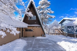 Ein schneebedecktes Chalet mit steilem Dach, Holzfassade und blauem Himmel.