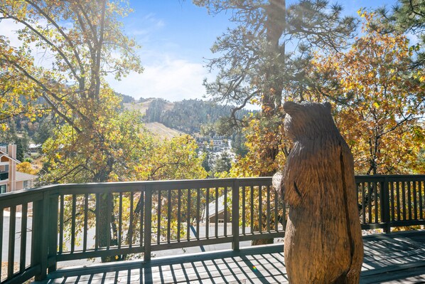 A wooden bear sculpture on a wooden deck with a view of a hilly landscape.