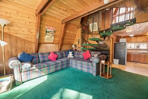 A cozy cabin interior with a plaid sofa, a small table, and a staircase.