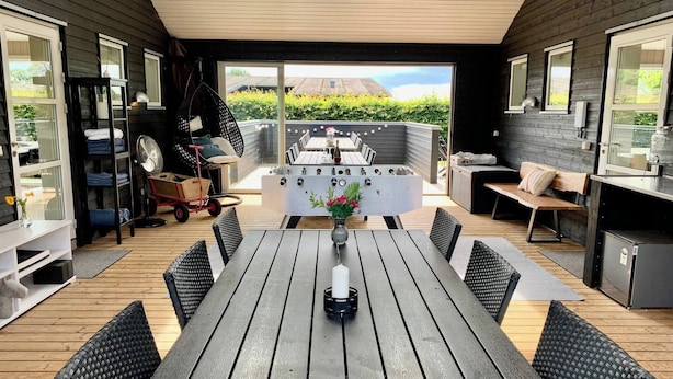A wooden deck with a dining table and chairs, a grill, and a seating area with a bench and cushions. - 2 Houses In One I Family Friendly I Kids I Sauna I Beach I Large Garden (Haderslev)