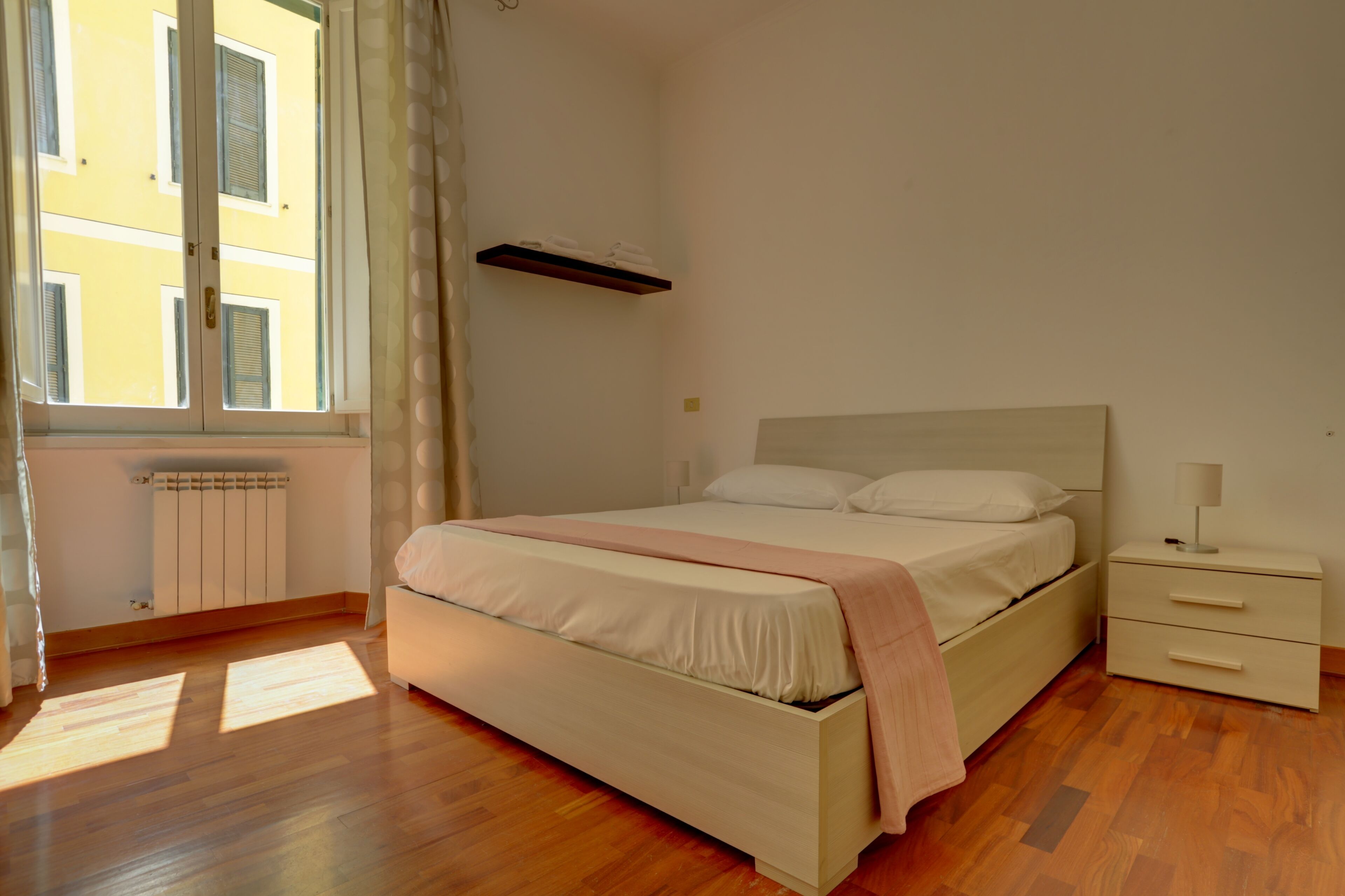 Un dormitorio con cama, mesita de noche y ventana con cortinas.