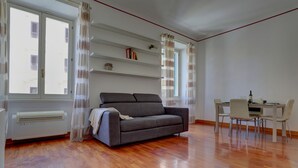 A living room with a sofa, dining table, chairs, and a window with curtains. - COLOSSEO Apt Mecenate 77 - Home and More (Rome)